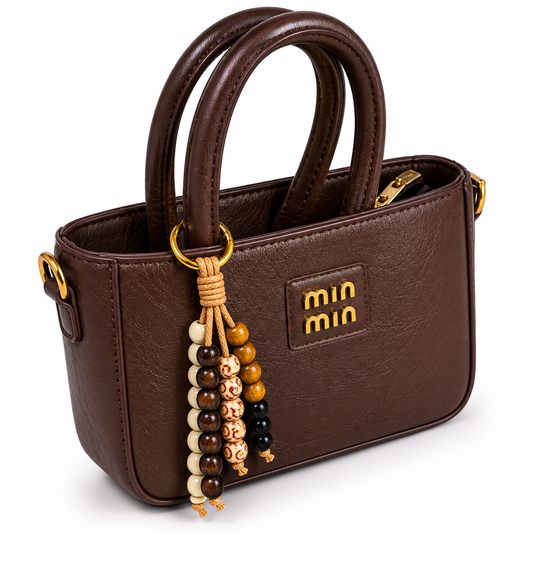 BOLSO MINI EN CUERO SINTÉTICO, CORREA AJUSTABLE, CIERRE INTERNO Y CHARM DE CHAQUIRAS.
